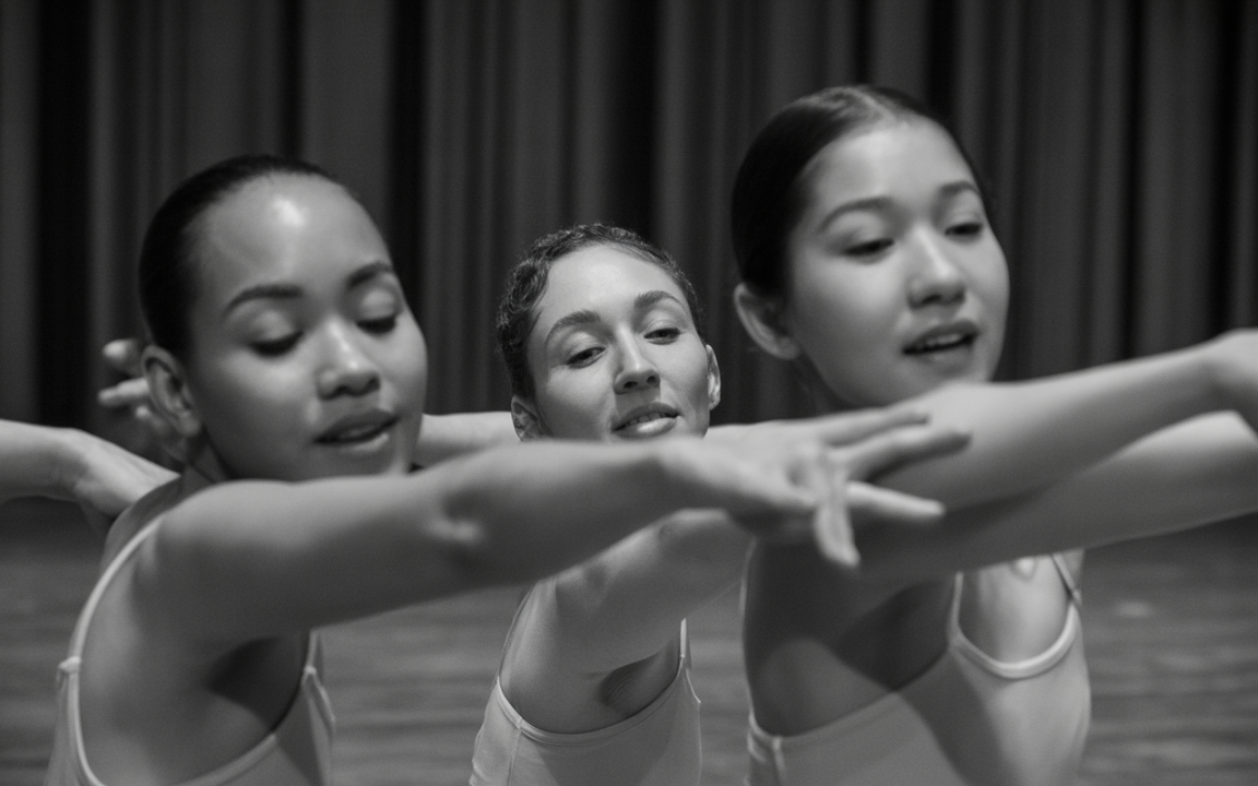 Trois danseuses exécutent une chorégraphie, bras tendus, exprimant grâce et concentration dans une ambiance monochrome.