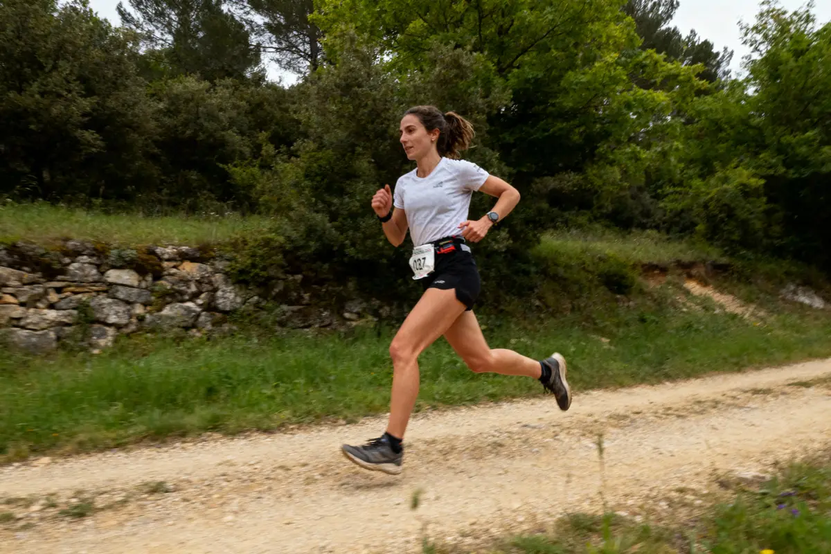 Une femme court sur un chemin de terre entouré de verdure, portant des vêtements de sport.
