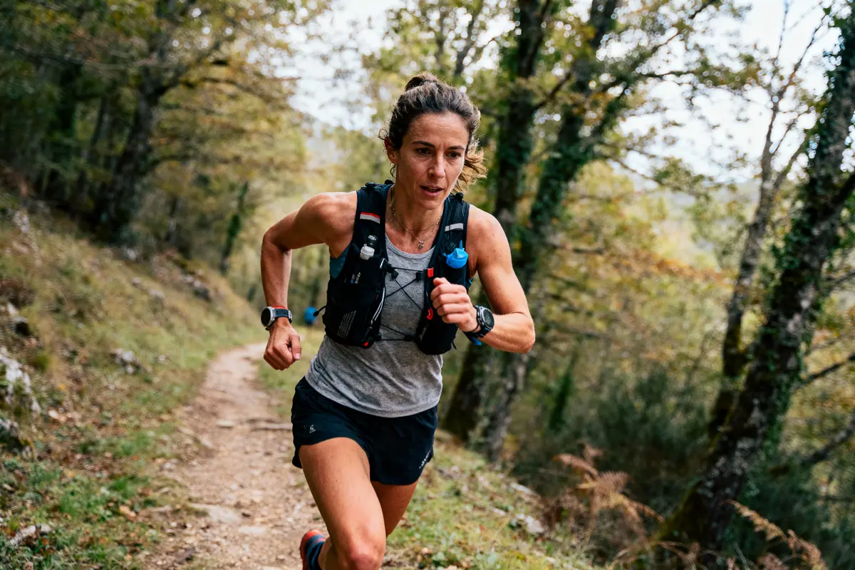Femme courant sur un sentier forestier, portant une montre et un gilet de sport noir.