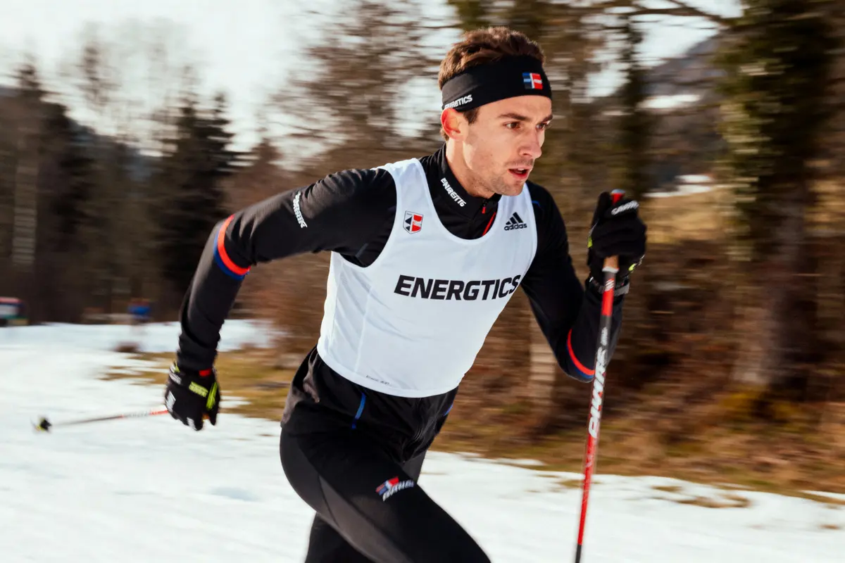 Skieur de fond en action sur la neige, portant une tenue de sport noire et blanche.