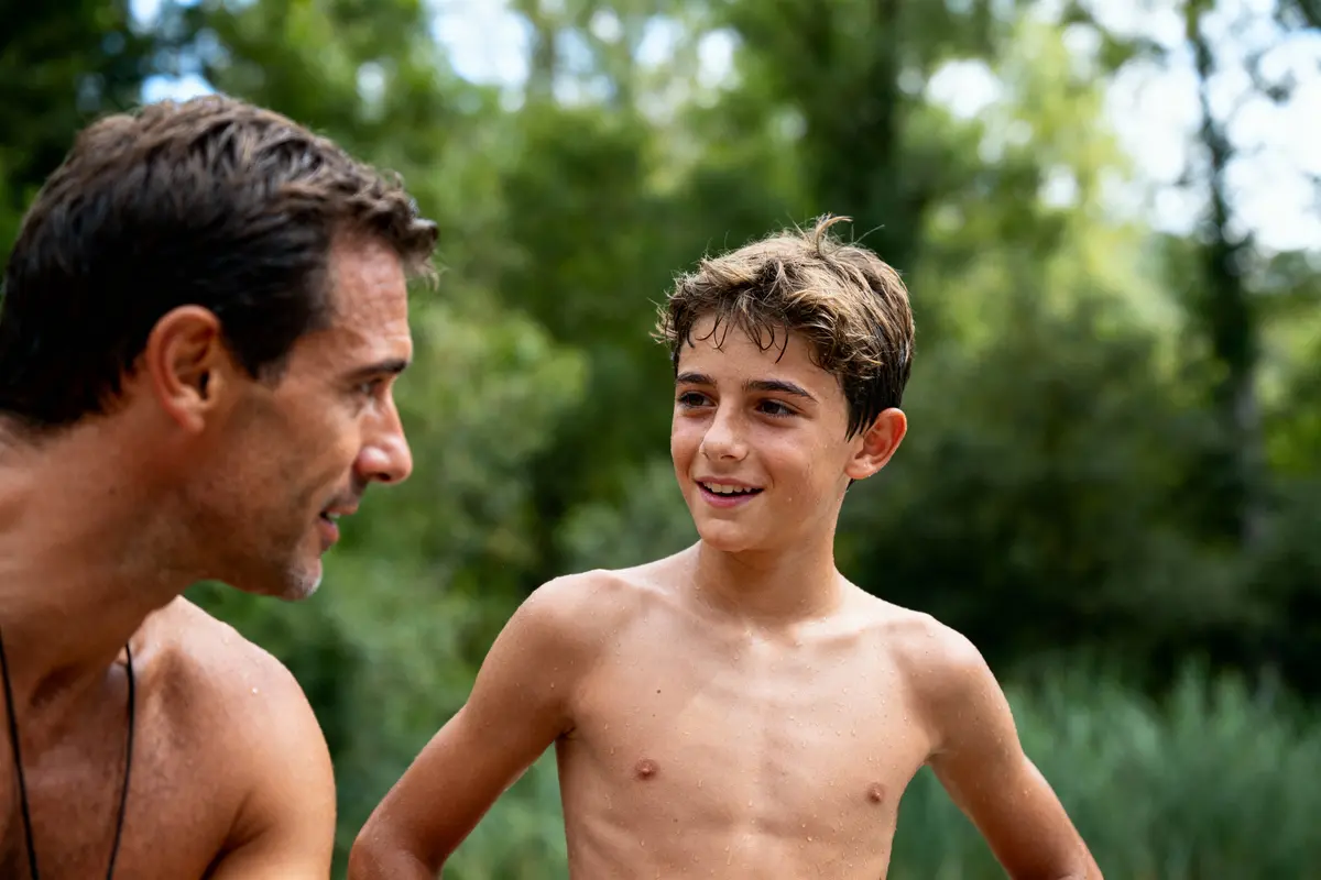 Homme et garçon souriant torse nu dehors, forêt en arrière-plan. Conversation amicale dans la nature.