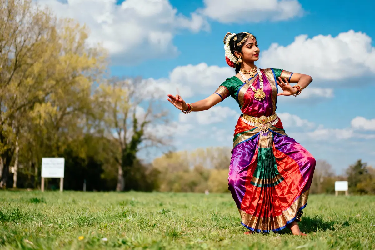 Femme dansant en plein air, vêtue de tenue traditionnelle colorée, ciel bleu en arrière-plan.