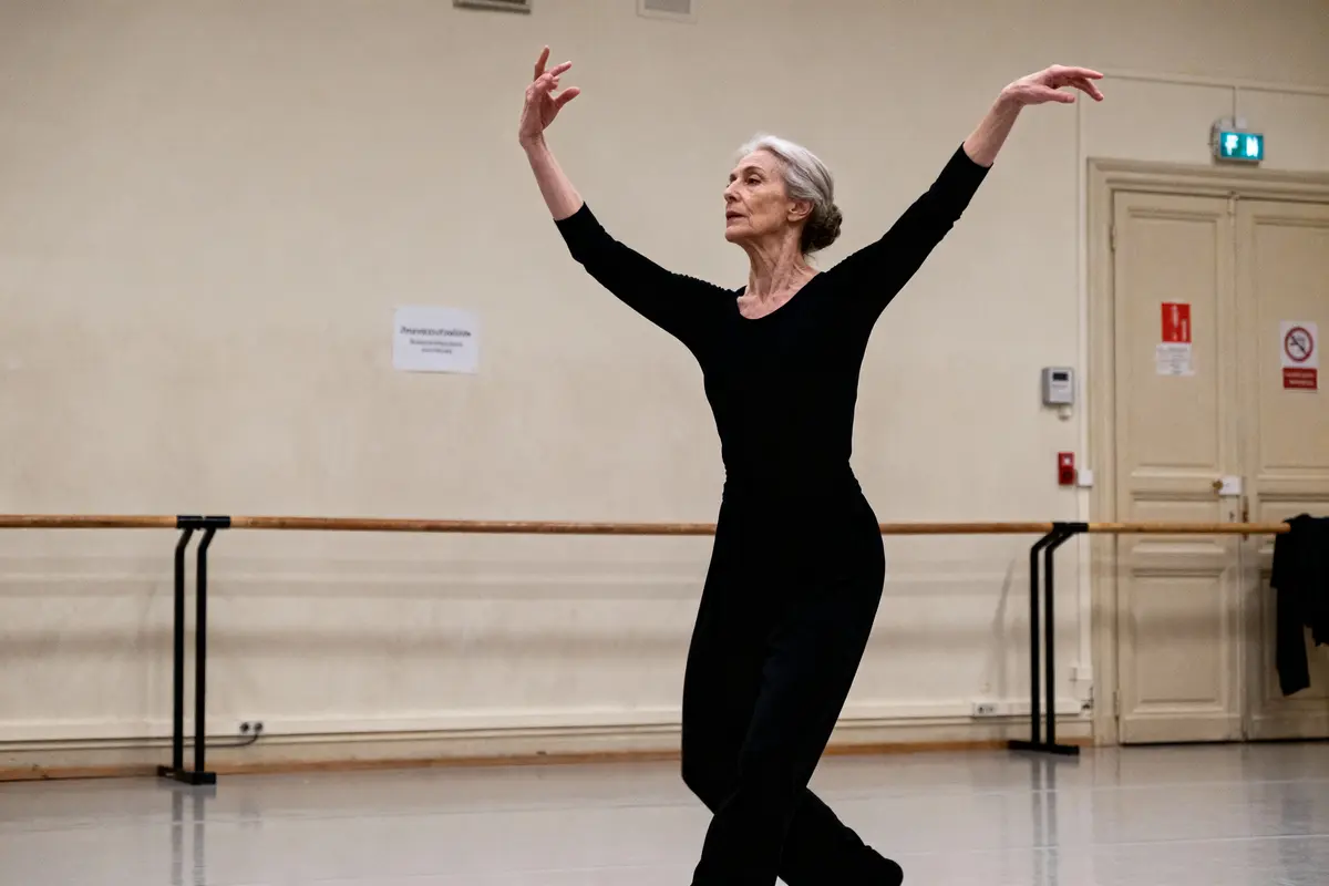 Danseuse en noir exécutant un plié dans un studio de danse, bras levés avec grâce.