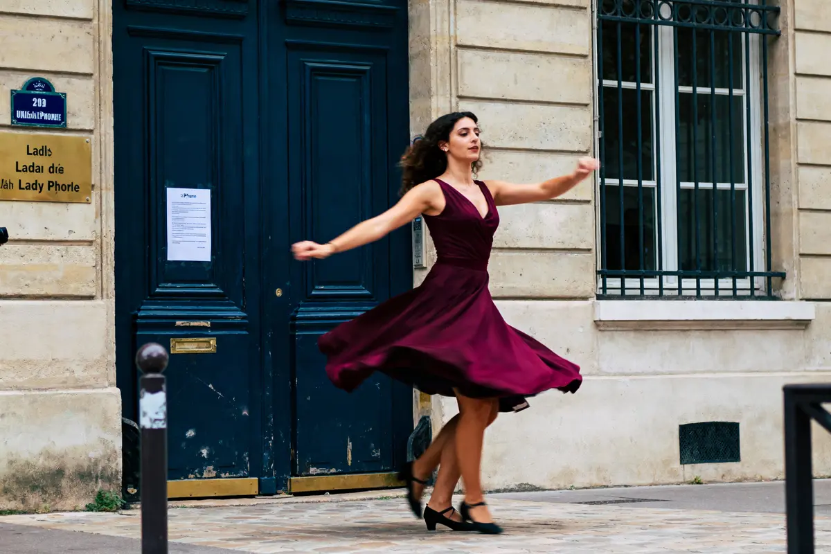 Femme dansant en robe bordeaux, devant porte bleue et mur beige.