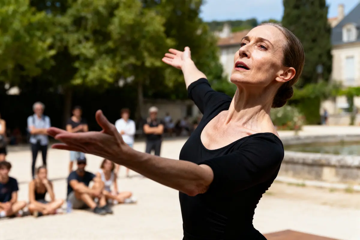 Danseuse vêtue de noir réalisant un mouvement gracieux en extérieur, public assis en arrière-plan.
