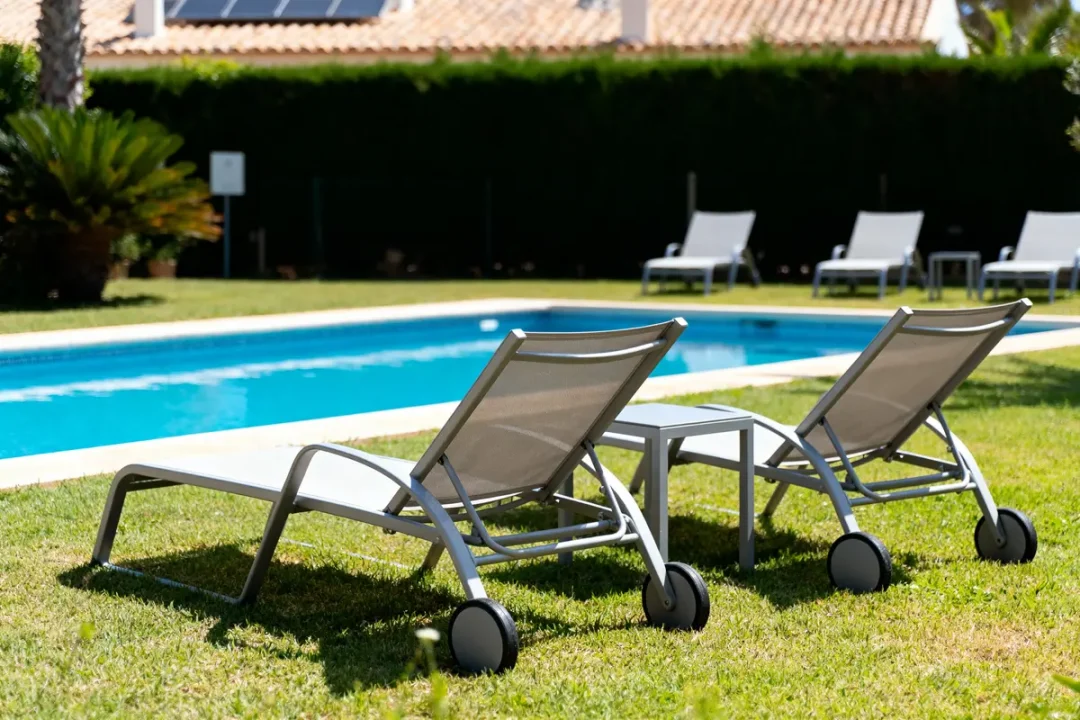 Deux chaises longues grises sur pelouse, près d'une piscine extérieure, journée ensoleillée.