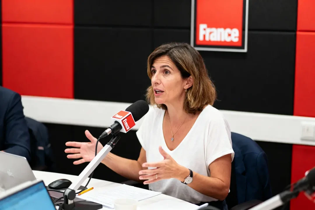 Femme parlant à la radio, micro France, décor rouge et noir, geste expressif, chemise blanche, studio.