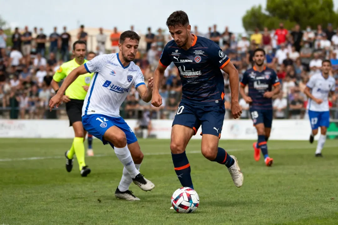 Deux joueurs de football en action sur le terrain, entourés d'autres joueurs et d'un arbitre.