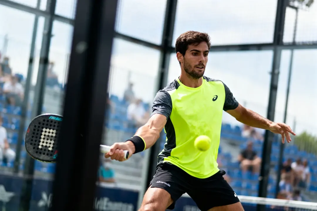 Joueur de padel concentré, frappe une balle sur un court extérieur, portant un maillot jaune vif.