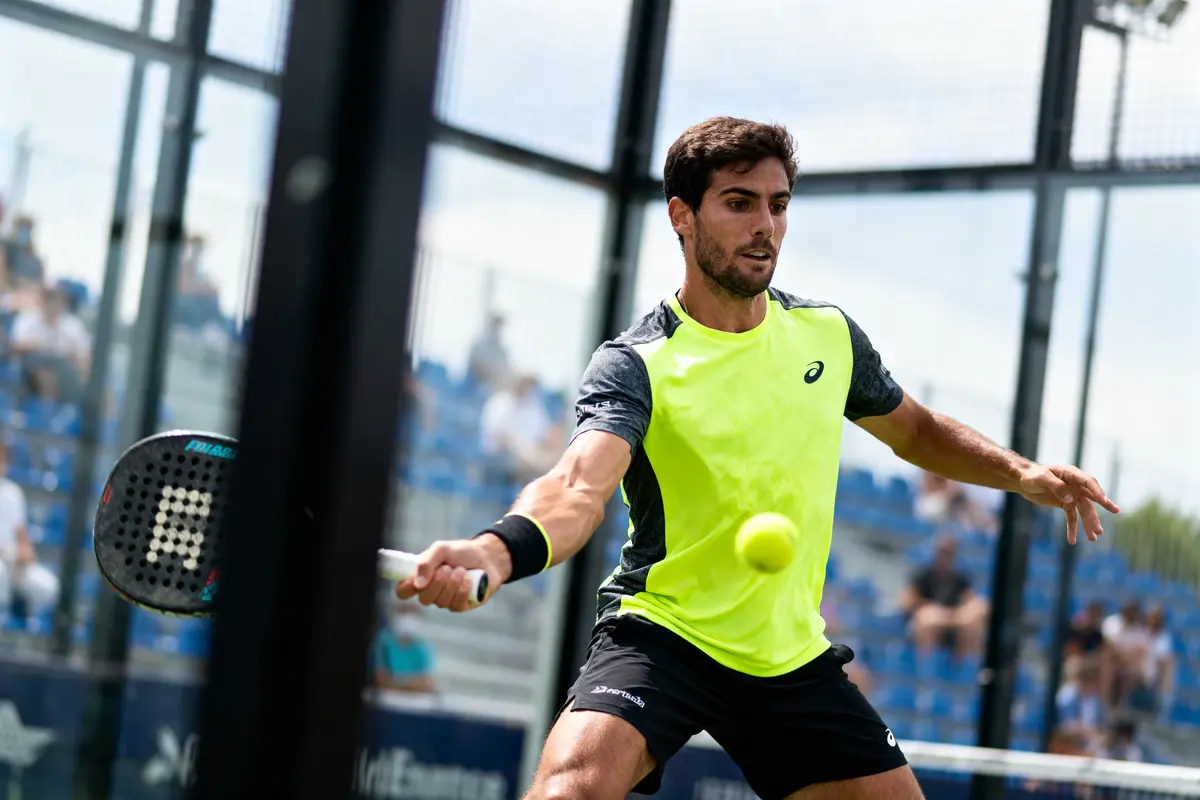 Joueur de padel concentré, frappe une balle sur un court extérieur, portant un maillot jaune vif.