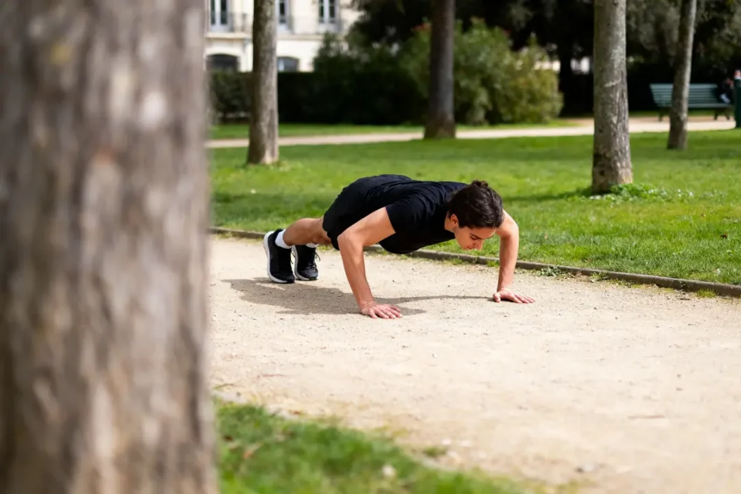 Homme en noir faisant des pompes sur un chemin de parc, entouré d'arbres et pelouse.