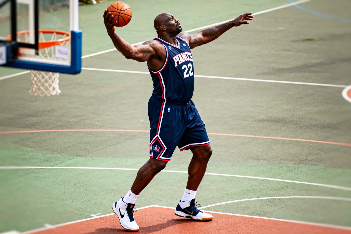 Joueur de basket en tenue bleue, tenant un ballon, sur un terrain extérieur près d’un panier.