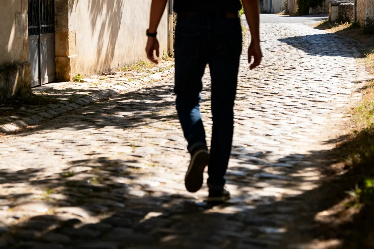 Personne marchant sur une rue pavée ensoleillée, ombres des arbres visibles, atmosphÚre d'été tranquille.