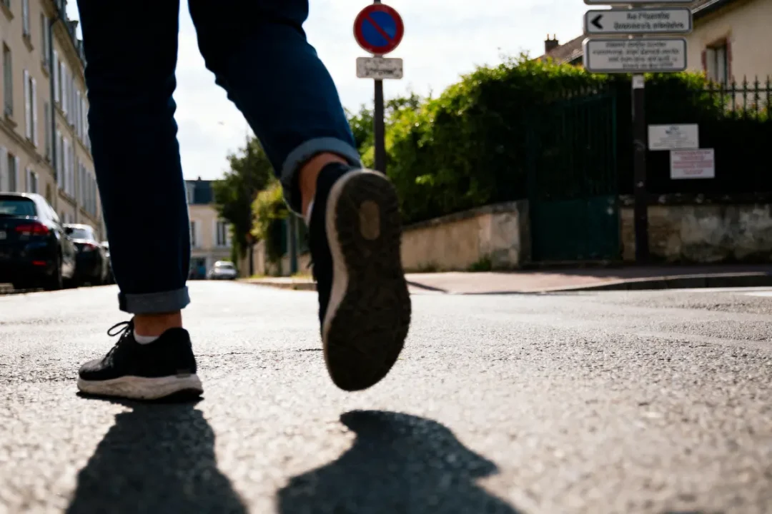 Personne marchant dans la rue, chaussée en baskets, ciel dégagé, panneaux routiers en arrière-plan.