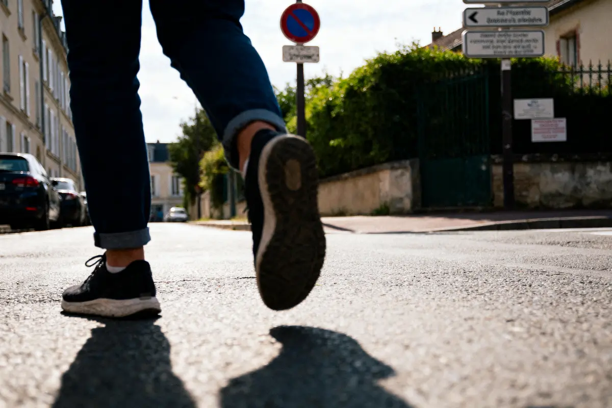 Personne marchant dans la rue, chaussée en baskets, ciel dégagé, panneaux routiers en arrière-plan.