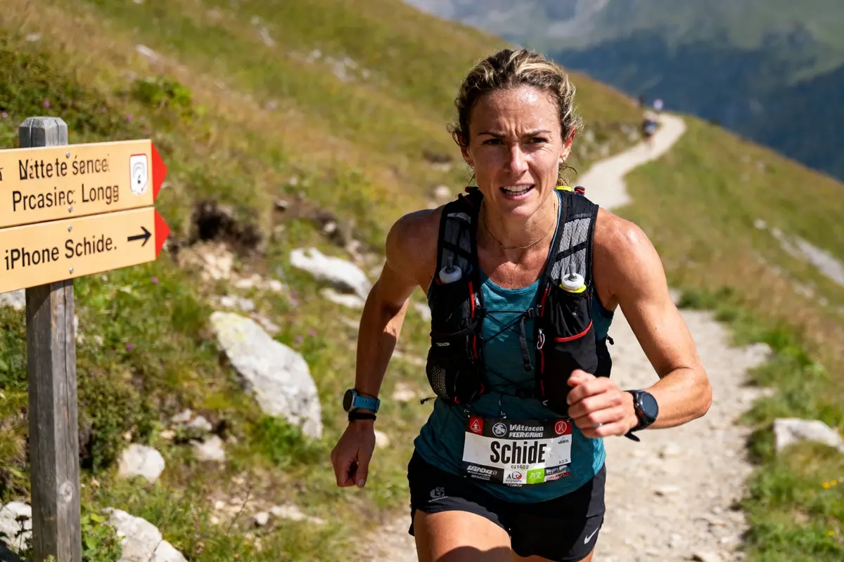 Coureuse en montagne avec dossard, chemin serpentant, panneau directionnel, environnement alpin, course d'endurance en plein air.