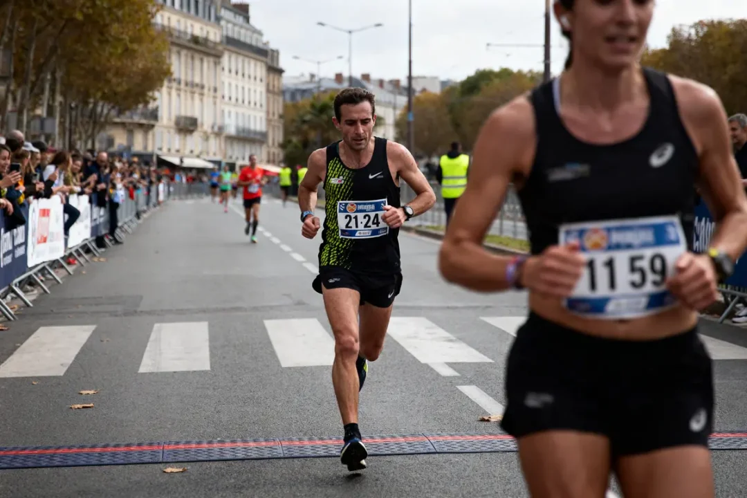 Deux coureurs en compétition lors d'un marathon urbain, entourés de spectateurs et bâtiments en arrière-plan.