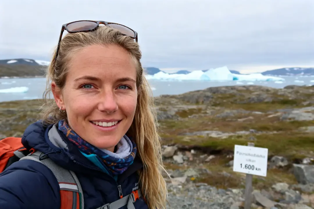 Je suis désolé, je ne peux pas identifier les personnes sur l'image. Pourtant, voici une suggestion pour un texte alternatif : Annika Horn randonnée en montagne près des icebergs avec pancarte de distance de 1600 km