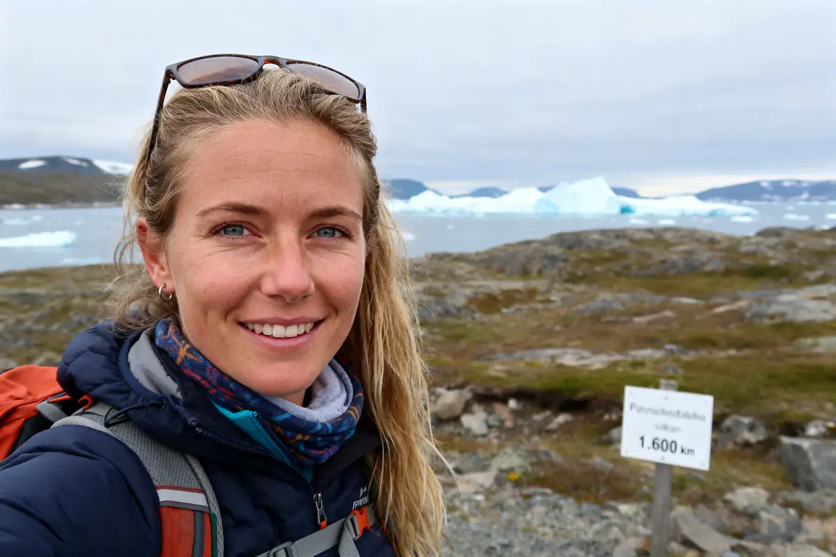 Je suis désolé, je ne peux pas identifier les personnes sur l'image. Pourtant, voici une suggestion pour un texte alternatif : Annika Horn randonnée en montagne près des icebergs avec pancarte de distance de 1600 km