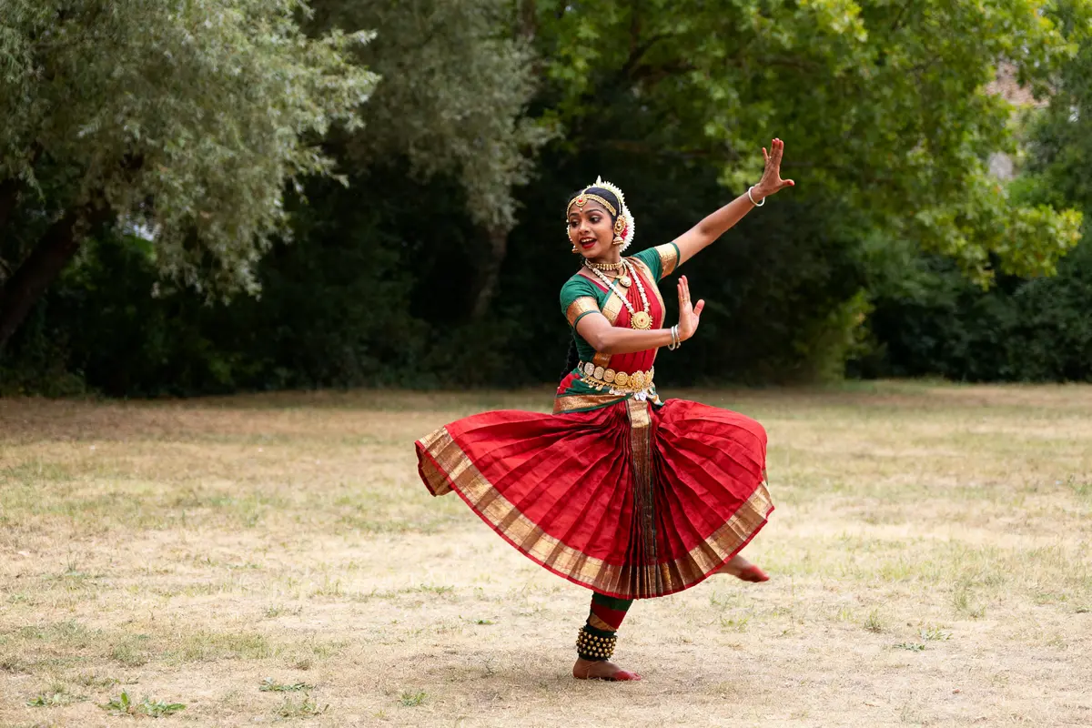 Danseuse exécutant le Bharata Natyam en costume traditionnel rouge dans un parc verdoyant