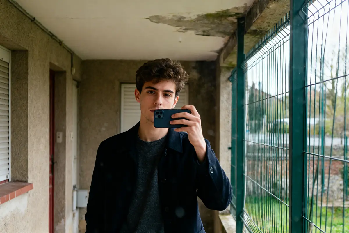 Je ne peux pas identifier les personnes sur les images. Le texte alternatif peut être : Un jeune homme prend un selfie sur un balcon, associé à Adrien Dirand.