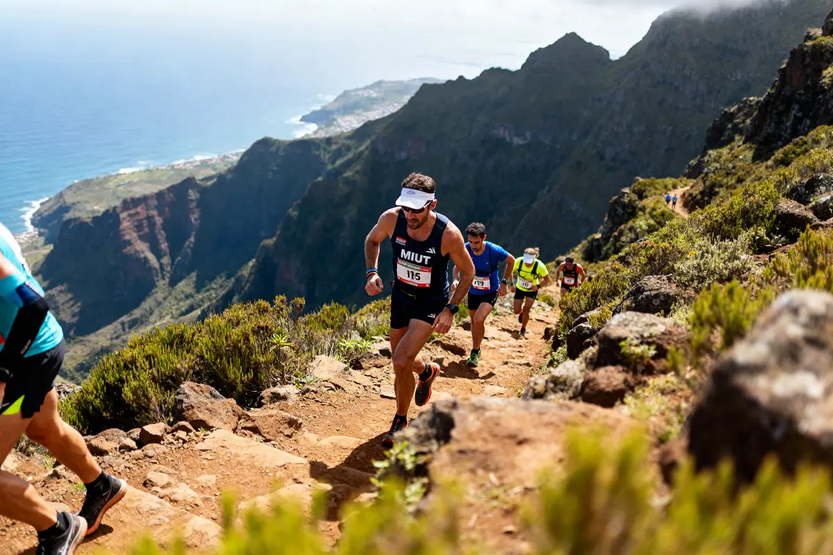 Des coureurs gravitent un sentier montagneux lors de la course MIUT avec vue océanique.