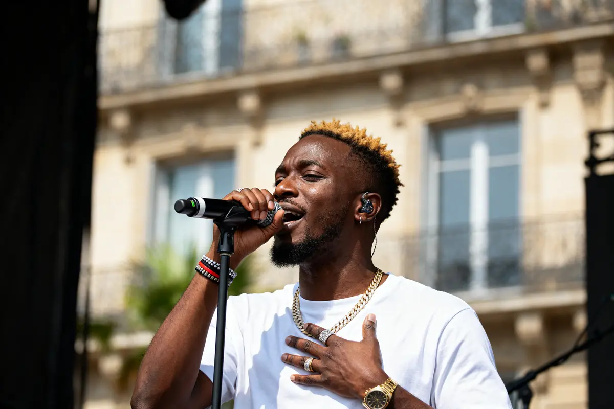 Chanteur africain interprétant une chanson sur scène en plein air à côté d'un immeuble