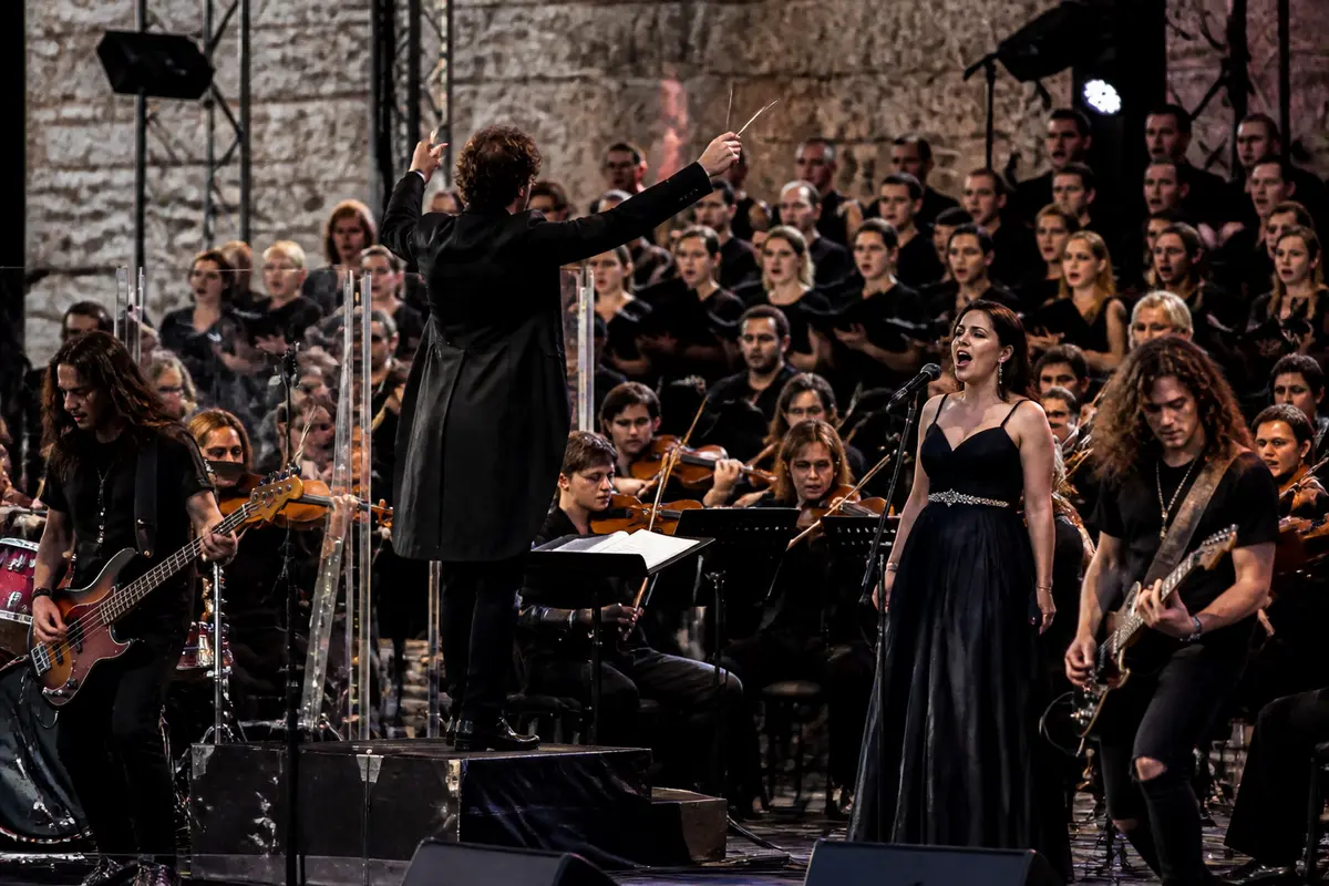 Chef d'orchestre dirige The Rock Symphony Orchestra en concert avec une chanteuse et des musiciens